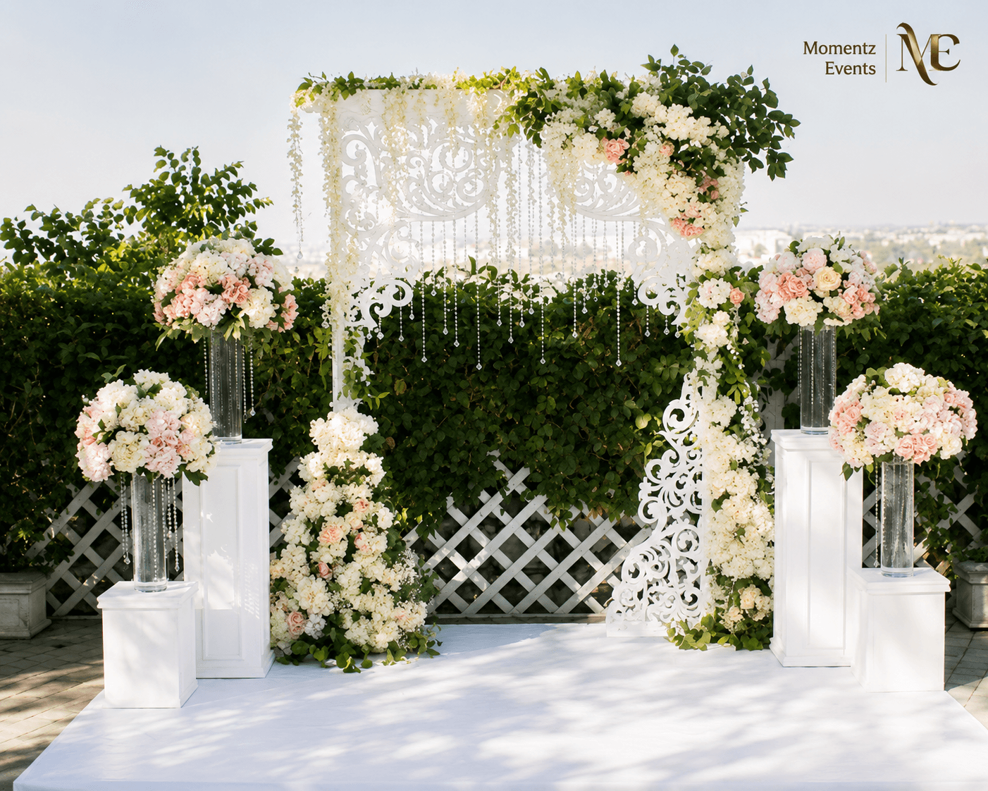Outdoor wedding ceremony arch with white lattice panel and greenery, styled by Momentz Events