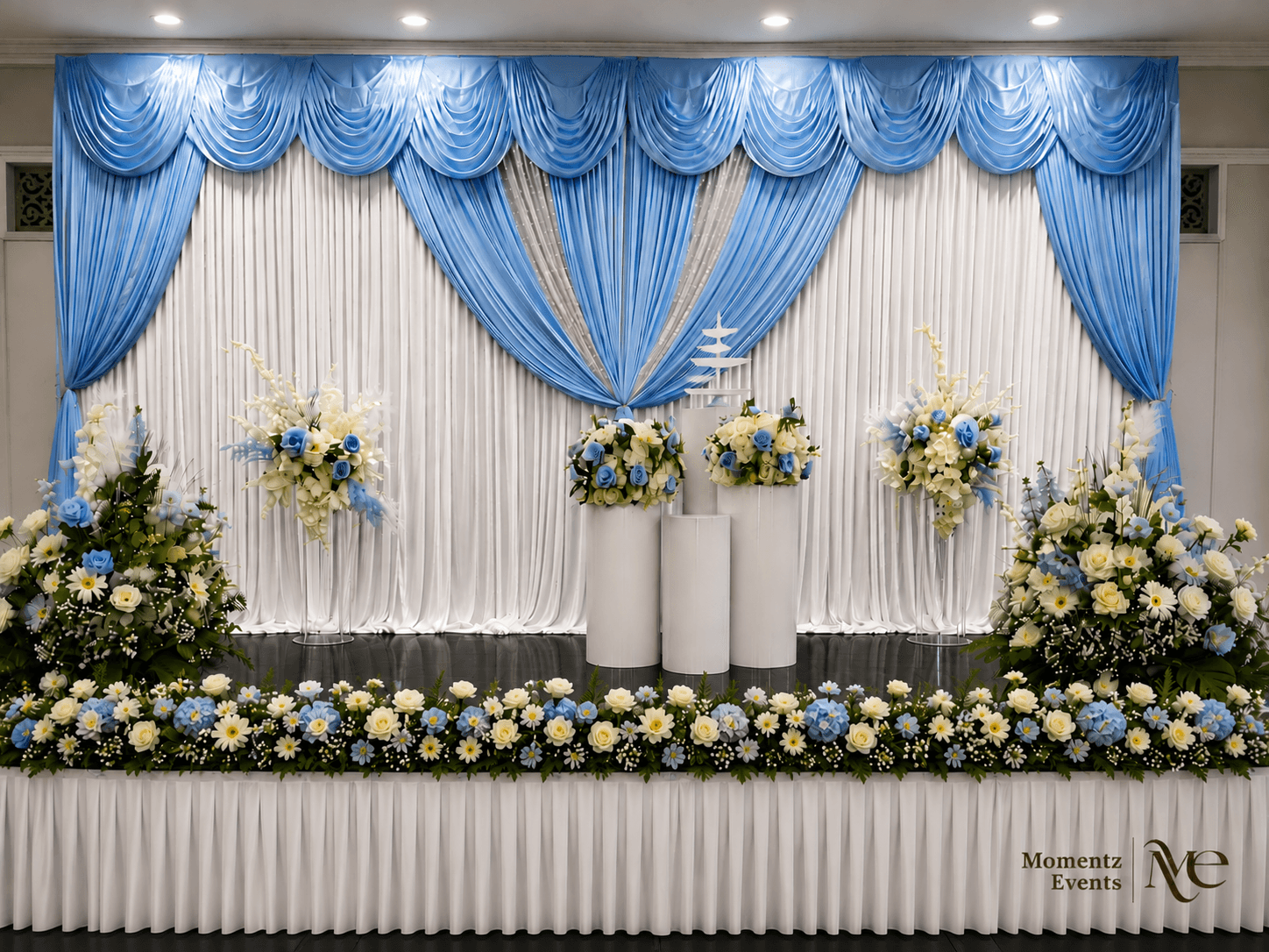 Elegant blue and white draped stage backdrop with floral accents, styled by Momentz Events