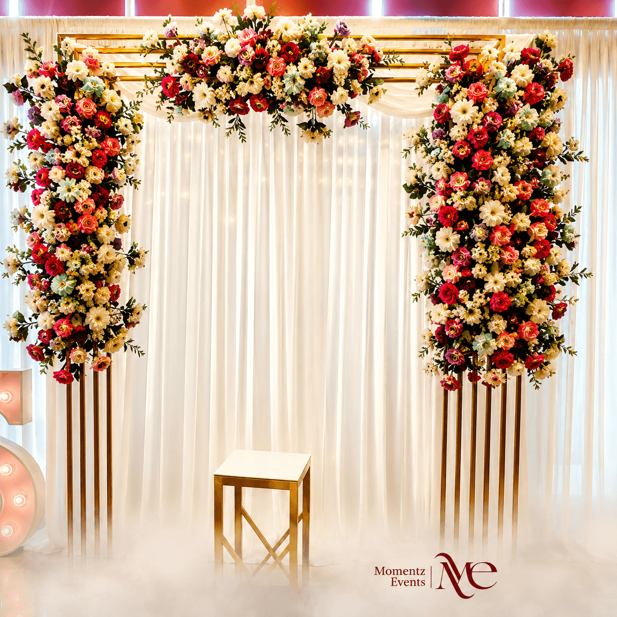 Elegant gold-framed floral arch backdrop in red, cream and gold tones, styled by Momentz Events